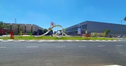 כיכר הספורט בעפולה: סרט נירוסטה מתפתל ודמויות צבעוניות של רוכבי אופניים וספורטאים, הדמיה