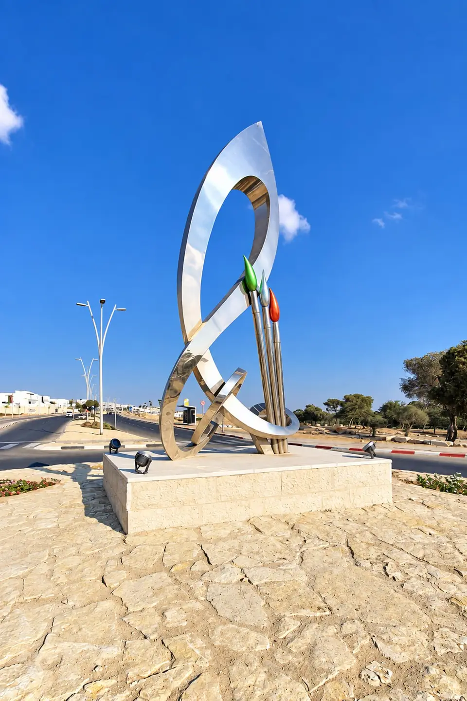מכחולים ומוסיקה: לולאות נירוסטה מלוטשת ושלושה מכחולים צבעוניים, על בסיס אבן בכיכר בדימונה