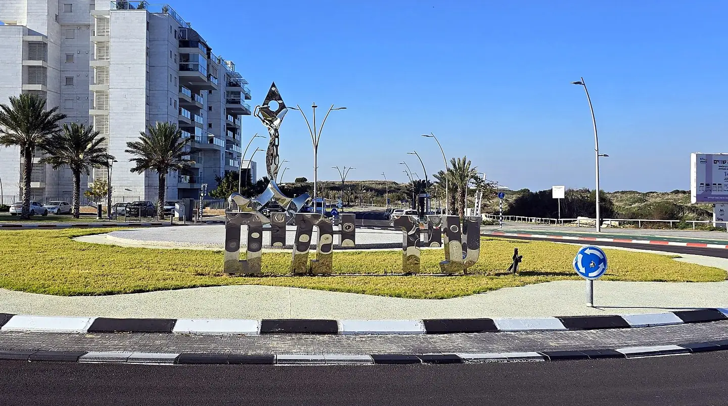 פסל נירוסטה מלוטש עם אותיות עבריות גדולות בכיכר ליד הים